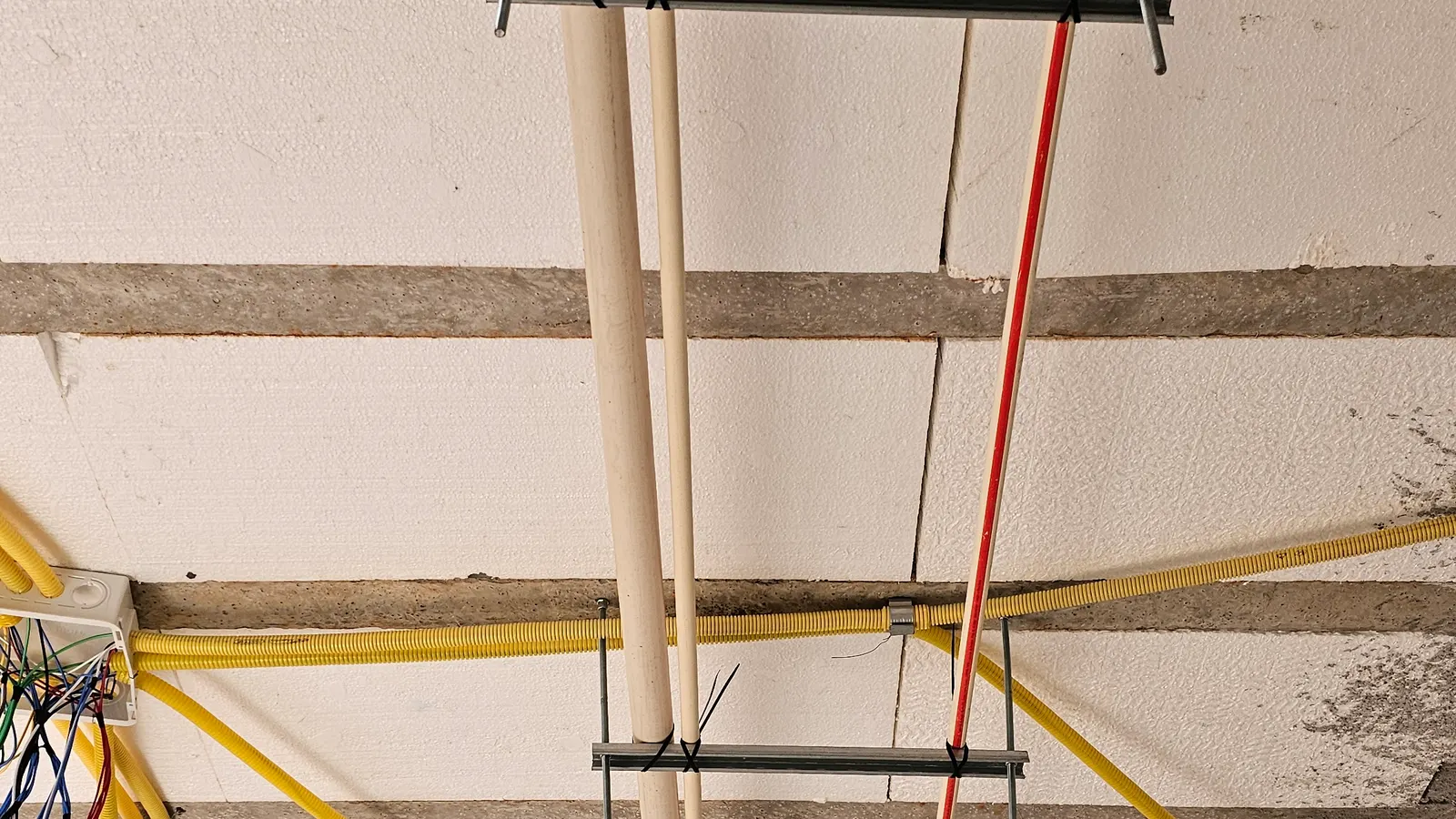 Tubulação de água quente (CPVC vermelho) e água fria/esgoto (PVC branco) presas com suporte metálico e barra roscada na laje treliçada, obra do Condomínio Campos do Conde