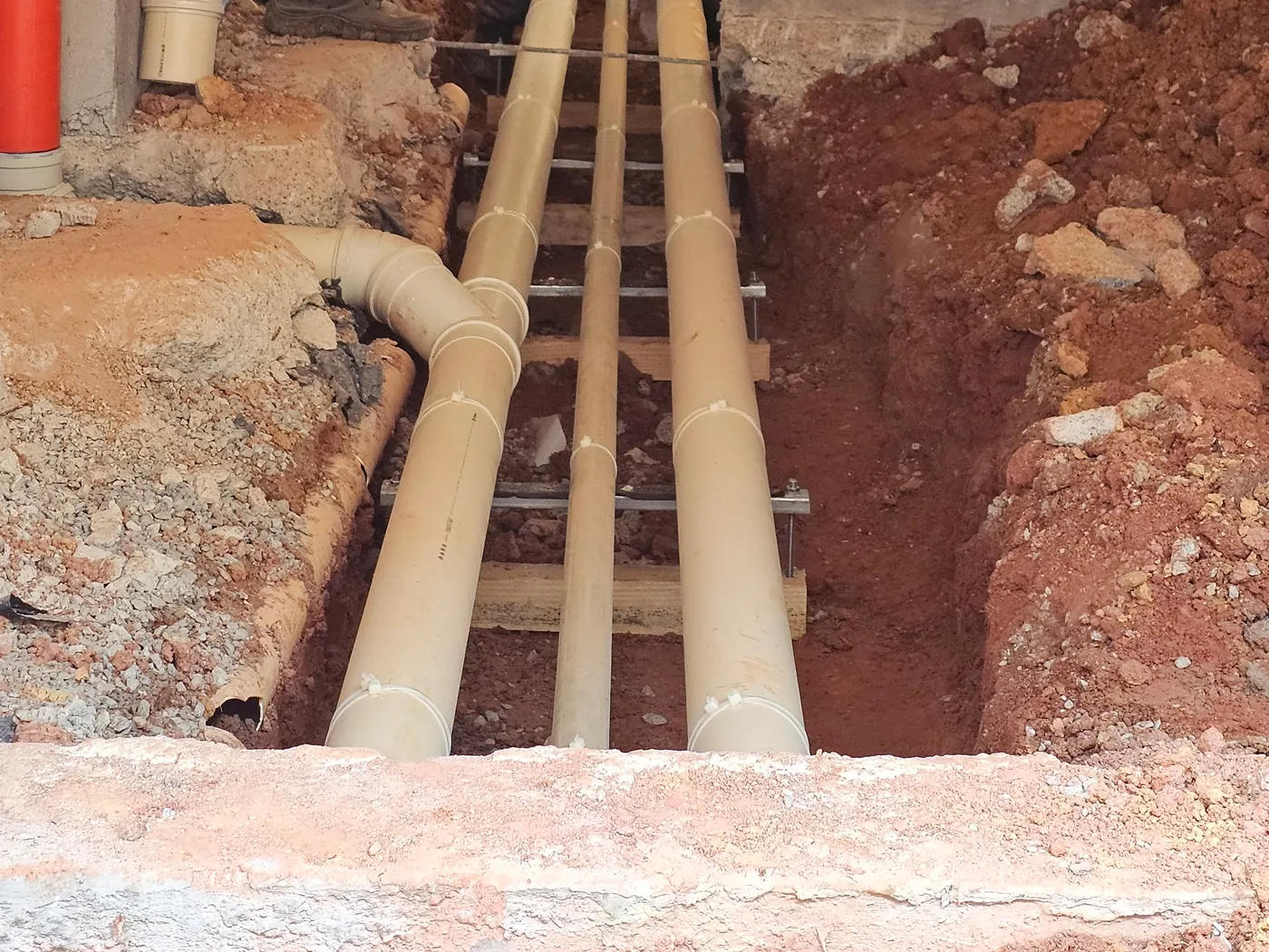 Três tubulações paralelas presas ao mesmo suporte metálico repetido ao longo da vala, obra do Portal Bragança
